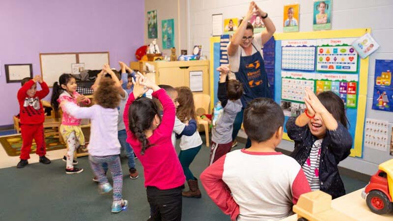 Teacher leads young children in an active classroom game, representing early education and childcare workforce development.